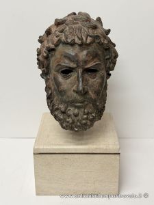 Elegante busto escultórico en bronce que representa a un personaje greco-romano sobre una base cuadrada de travertino.
