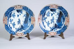 A pair of Japanese porcelain plates decorated with flowers and stylised ocean waves in blue and whit