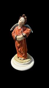 Estatueta de porcelana com figura de anjo tocando acordeão. Assinatura: Gino Pezzato. Capodimonte.