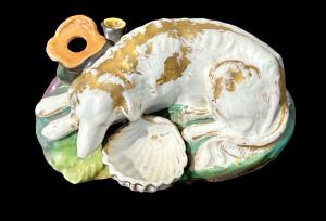 Calamo polícromo de porcelana que representa un perro agachado. Francia.