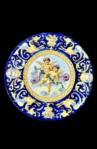 Piatto in maiolica policroma con al centro coppia di cherubini e tesa a grottesche. Manifattura Battaglia.Napoli.