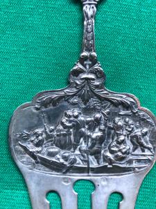 Garfo de prata repoussé com figuras em um barco, máscaras e motivos vegetais estilizados. Holanda 1860.