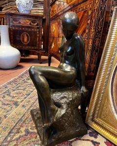 Female nude bronze by Audagna Virgilio (1903). The woman is depicted sitting on a rock that serves as the base of the sculpture. The arms are outstretched, the torso is arranged frontally. The face is shown in profile with the hair gathered.