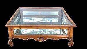 Mesa de centro vitrine para sala de estar em nogueira com tampo e laterais em vidro e base espelhada.