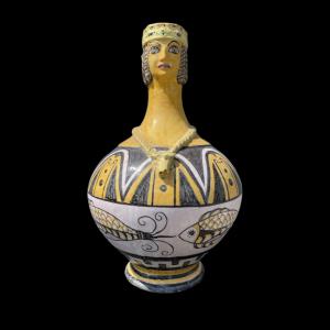 Majolika-Gießgefäß mit anthropomorpher Figur und geflochtenem Henkel. Sizilien.