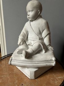 Scultura in marmo bianco di un bambino seduto