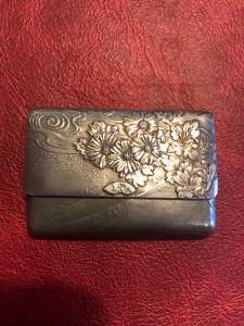 Scatolina portafiammiferi in metallo a forma di borsa-portafoglio con decori floreali art-nouveau.