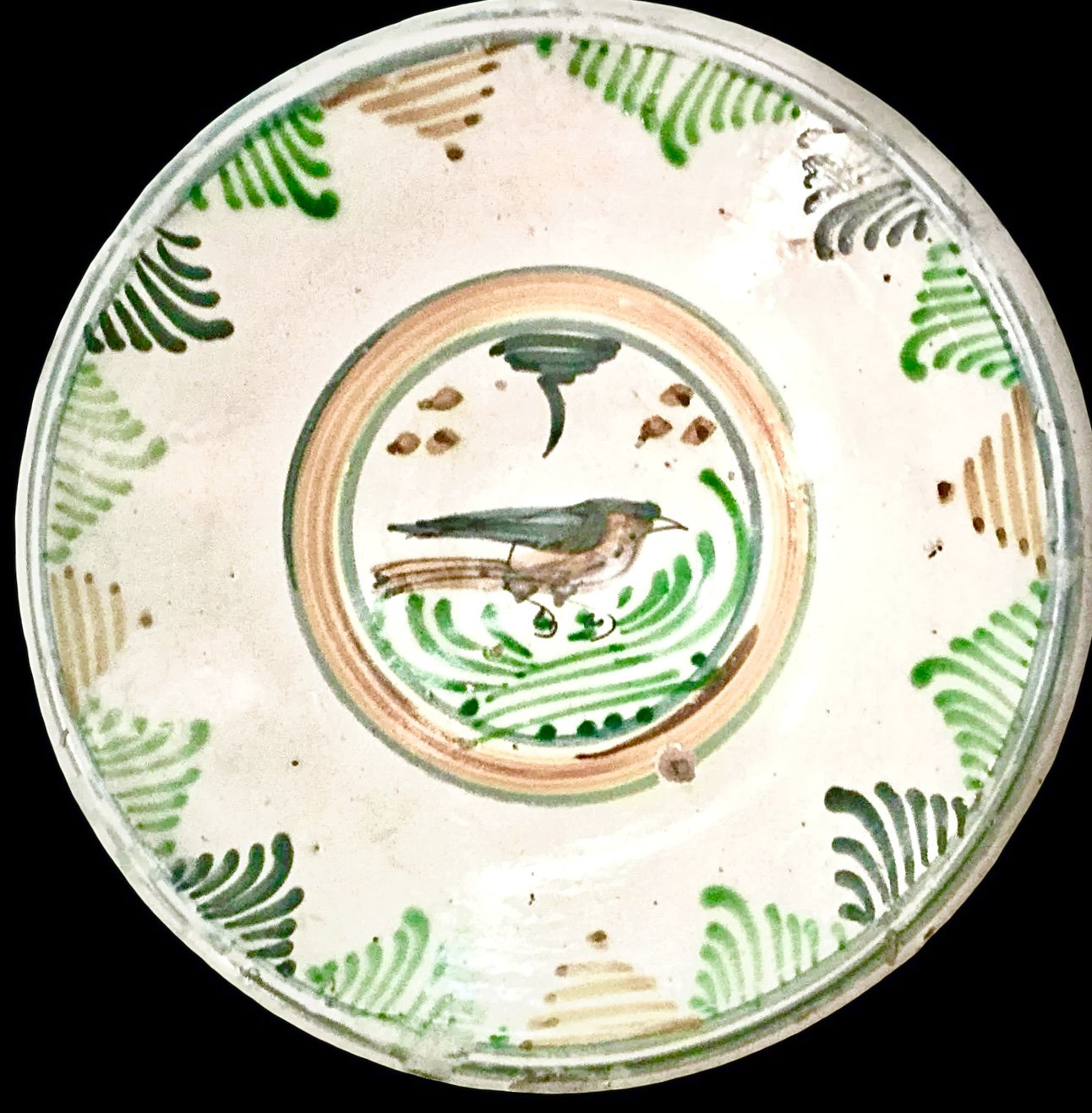 Assiette en faïence avec motifs végétaux stylisés sur le bord et oiselet au centre. Montelupo.