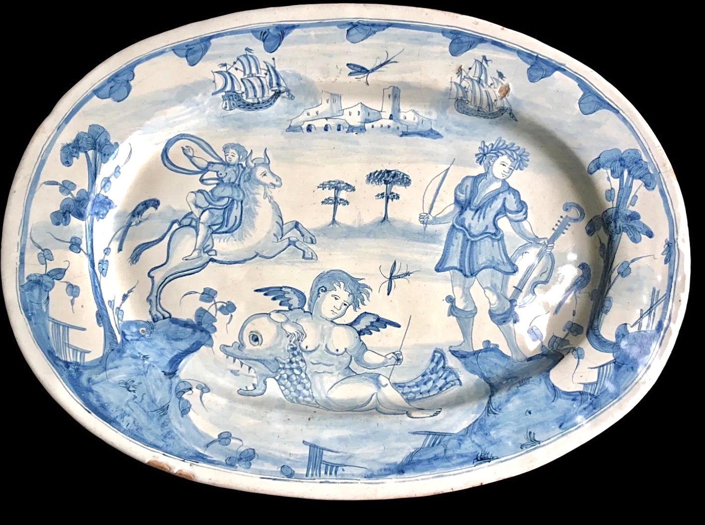Grande prato oval em majólica monocromática turquesa decorado com personagens e arquiteturas. Manufatura de Deruta.