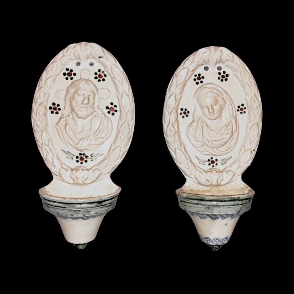Pair of earthenware holy water fonts with raised faces of Jesus and Mary and a border with plant motifs, Veneto.