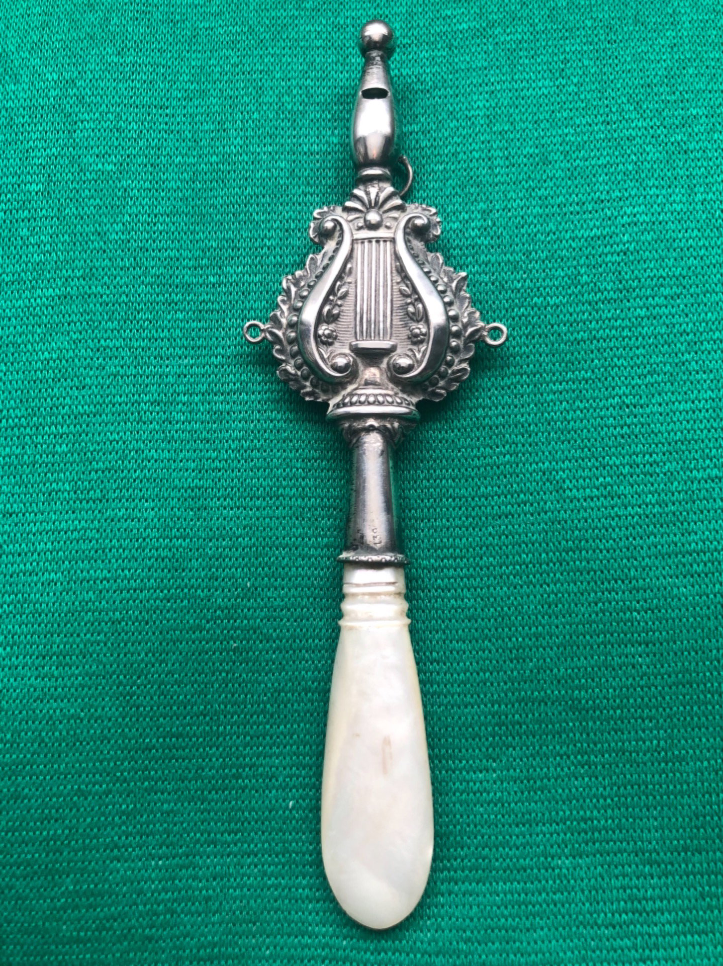 Silver baby rattle with stylized floral motifs and lyre. Mother-of-pearl handle.