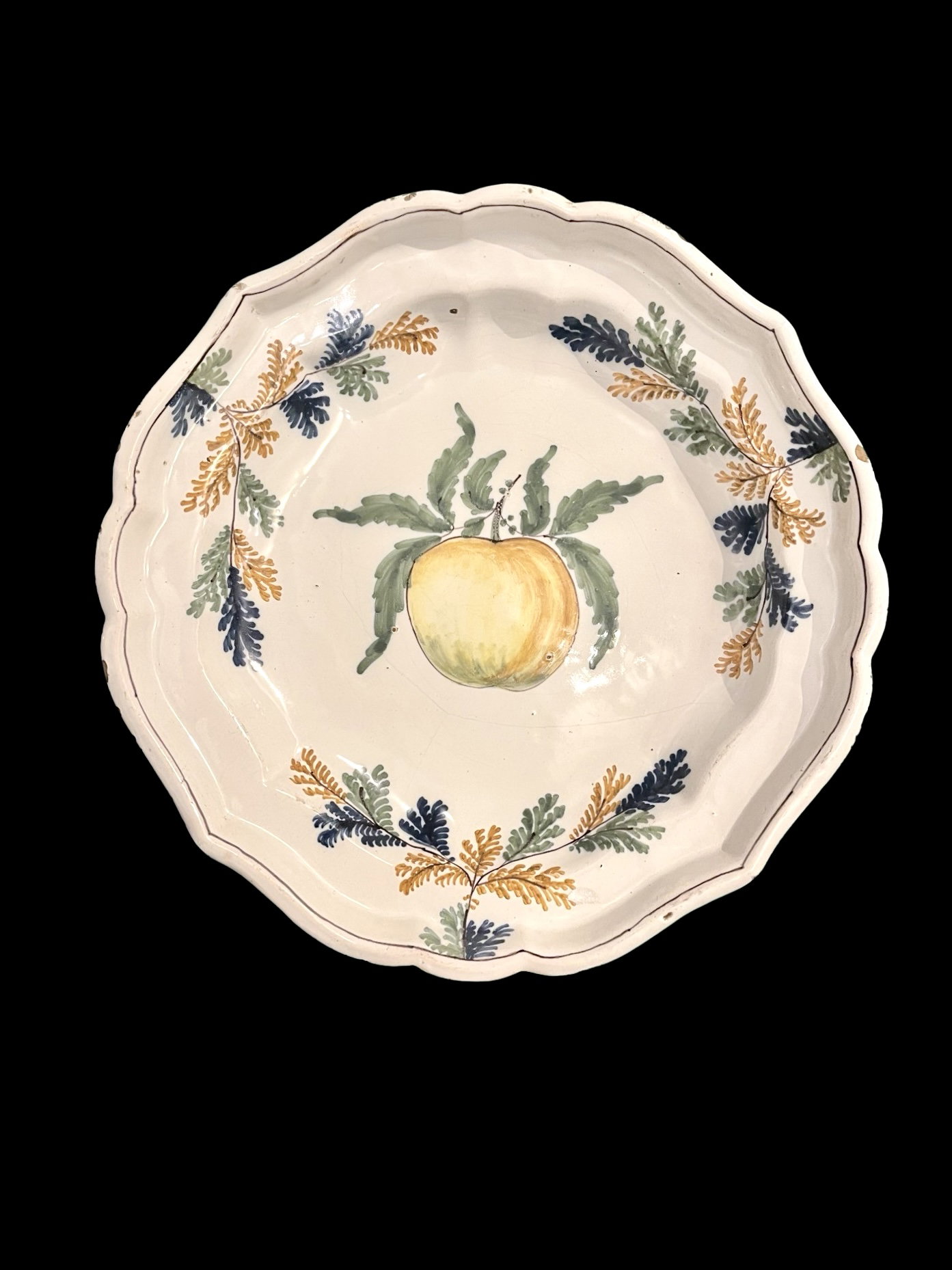 Plato de mayólica con fondo adornado con racimos vegetales en el borde y una fruta en el centro. Pavia.