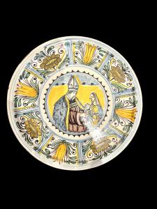 Maiolica plate with stylized floral motifs and a central depiction of a blessing bishop with mother and child. Manufacture of San Quirico d’Orcia.