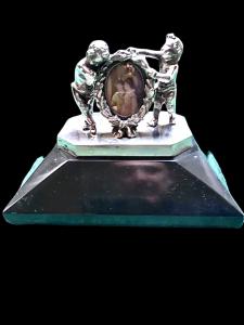Fermacarte de prata com dois querubins segurando um porta-retratos com miniatura.