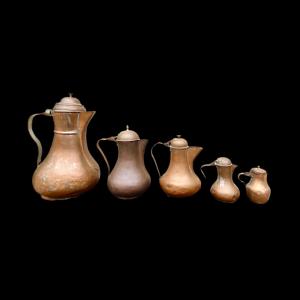 Series of five copper coffee pots of different sizes.