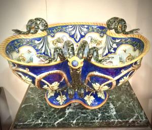 Centro de mesa trilobado em cerâmica policromada com desenhos rafaelescos e grotescos e um par de querubins no umbo. Três pegas em forma de serpente. Ginori, Sesto Fiorentino.