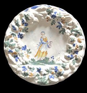 Maiolica plate with raised flower border and decoration featuring a female figure with a pouring vessel. Baldassarre Caravaggio. Pavia.