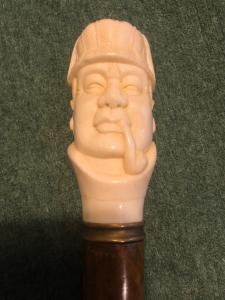 Bastone con pomolo in osso raffigurante figura maschile con cappello e pipa. 
